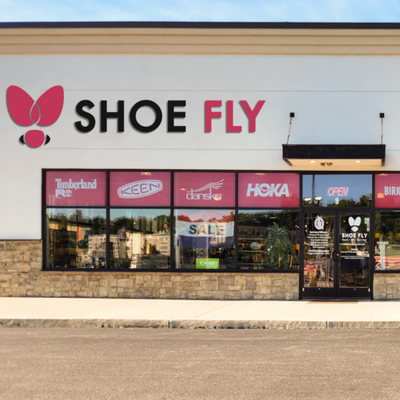 A shoe store named Shoe Fly with a butterfly logo on its sign; store brands like Timberland, Keen, Dansko, and Hoka are visible in the front windows, along with a SALE sign.